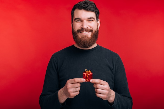 Take this small gift Smiling bearded man is holding a red little gift in his hands.