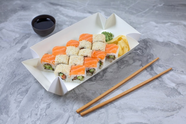 Takeaway box with sushi rolls on stone table.