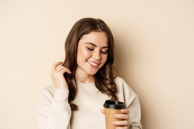 Concetto di caffè e da asporto. bella donna femminile sorridente, tenendo una tazza di caffè, in posa su sfondo beige