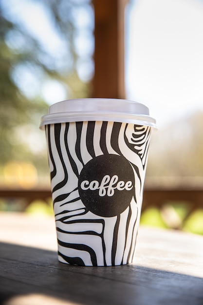 Photo takeaway disposable cup with coffee on wooden bench in morning garden