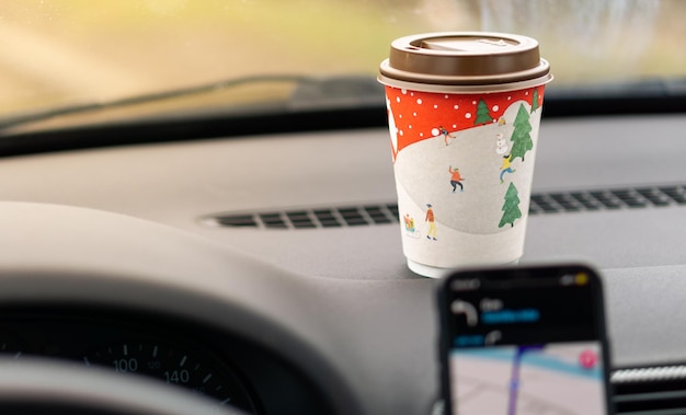 Takeaway paper cup with coffee in front of the car and navigation in the phone