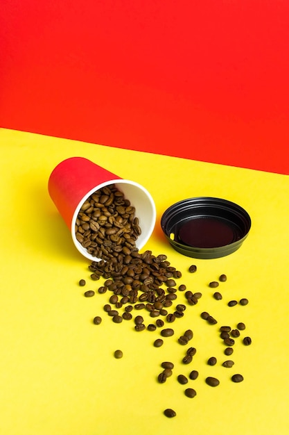 Takeaway red paper coffee cup with black cap on red and yellow background with pouring roasted beans