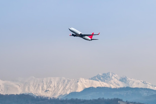 Decollo di un aereo di linea passeggeri sullo sfondo di alte montagne coperte di neve