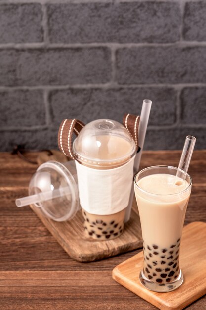 Еда на вынос с концепцией одноразового предмета популярный тайваньский напиток пузырьковый чай с молоком с пластиковой чашкой и соломкой на фоне деревянного стола, крупным планом, копией пространства