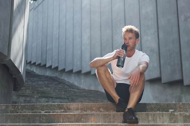 Takes a break Young man in sportive clothes have workout outdoors at daytime