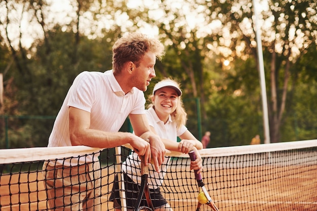 Fare una pausa appoggiandosi alla rete. due persone in divisa sportiva giocano a tennis insieme sul campo.