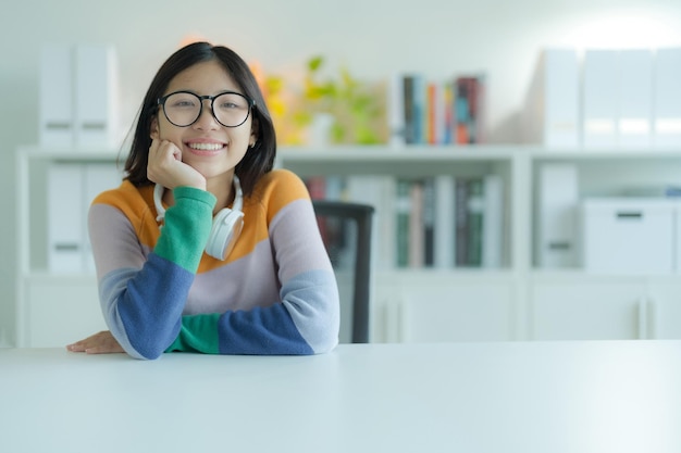 Taking a break from studying in the library is a smiling young woman or student wearing eyeglasses