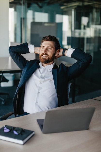 Taking break from work Excited businessman relaxing on chair leaning back at workplace and holding hands behind head