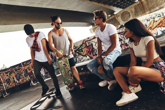 Taking a break. Group of young modern people talking while spending time at the skateboard park outdoors