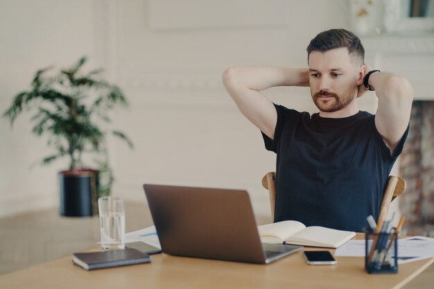 Taking a break. Male freelancer or entrepreneur in relaxed pose wearing casual clothes watching video or read information on laptop computer while working from home or modern office space