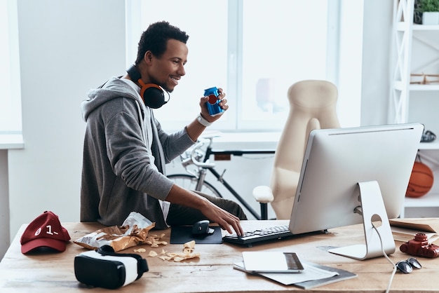 Taking a break. Relaxed young man in casual clothing smiling and typing something while spending time at home