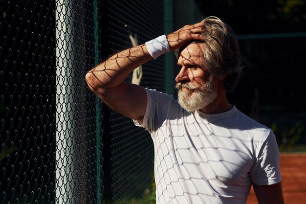 Photo taking a break senior modern stylish man outdoors on the sportive field at daytime