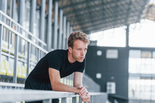 Taking a break Sportive young guy in black shirt and pants outdoors at daytime