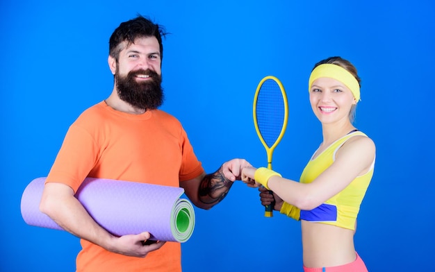 Taking a break Sporty couple training with fitness mat and tennis racket Strong muscles and body Happy woman and bearded man workout in gym Sport equipment Athletic Success break in training