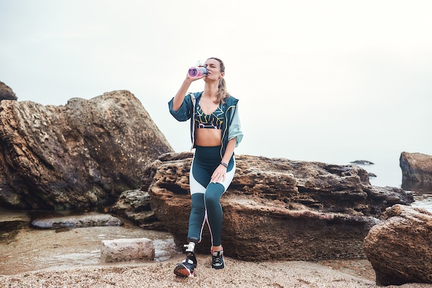 Taking a break tired disabled athlete woman with prosthetic leg drinking water while sitting on