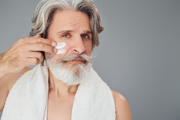 Taking care of face and skin clearness Stylish modern senior man with gray hair and beard is indoors