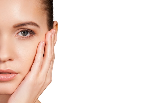 Taking care of her face. Cropped image of beautiful young woman holding hand on cheek and looking at camera while isolated on white background