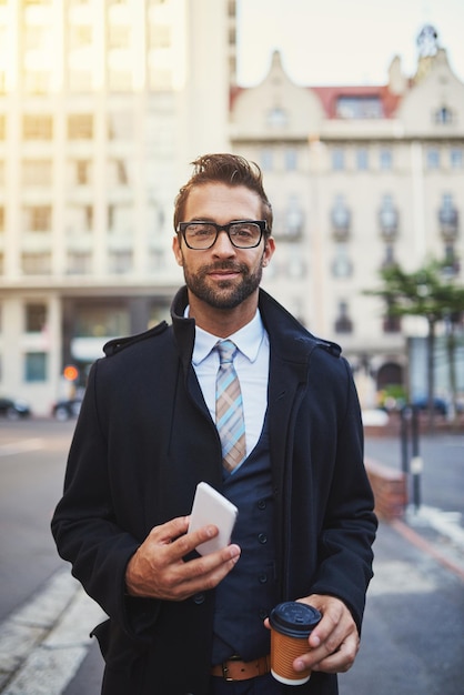 Portare il suo stile per le strade ritratto di un uomo alla moda con caffè e telefono in mano mentre è fuori città