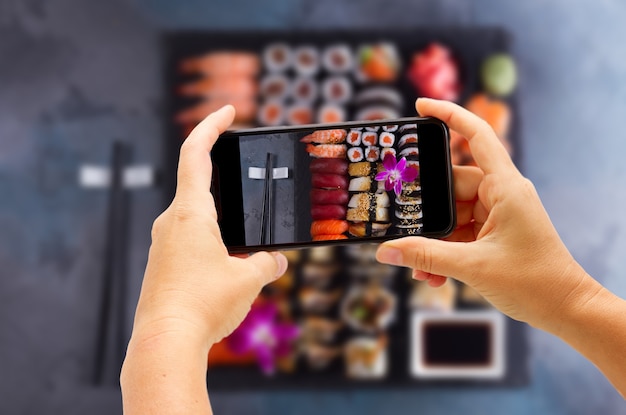 Taking photo of Japanese sushi big set with wooden black chopsticks on gray
