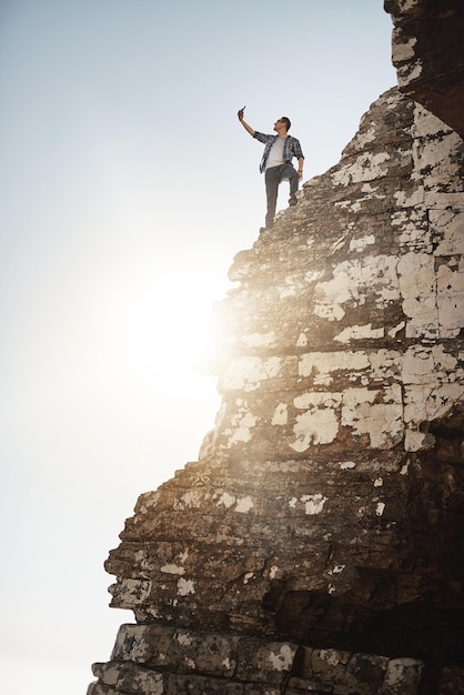 Taking a photograph from high altitude Shot of a young man taking photographs while standing on the edge of a mountain cliff