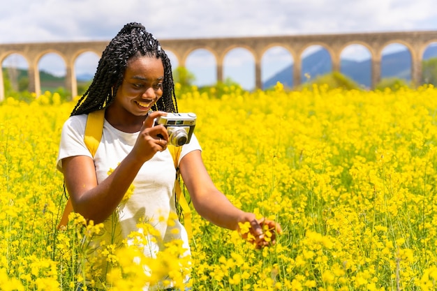 Taking photos with a vintage camera a black ethnic girl with braids a traveler in a field of yellow flowers