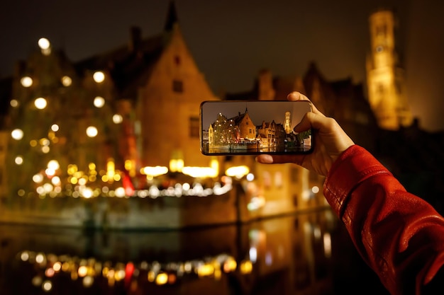 Foto scattare una foto della città vecchia belga di brugge illuminata di notte turista con smartphone