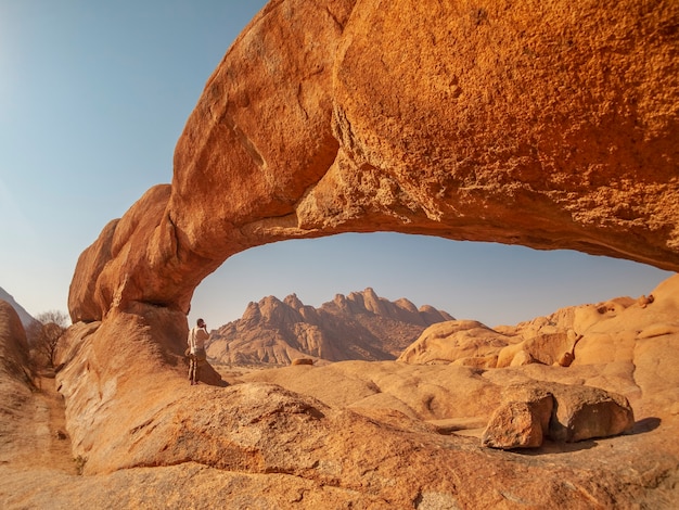 아프리카 나미비아의 스피츠 코페 국립 공원 (Spitzkoppe National Park)에있는 바위 아치 아래에서 사진을 찍고 있습니다.