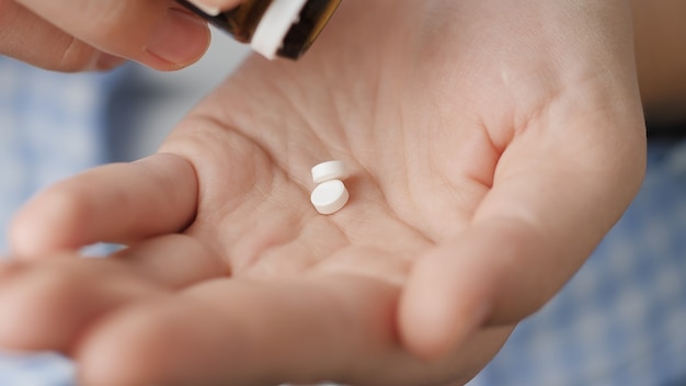 약 복용. 두 개의 작은 흰색 둥근 알약이 알약 병에서 손바닥에 떨어집니다. 클로즈업, 정면도, 중앙 구성