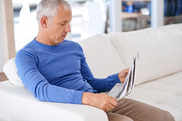 Найдите время, чтобы узнать новости Снимок зрелого мужчины, сидящего на диване в гостиной и читающего газету.