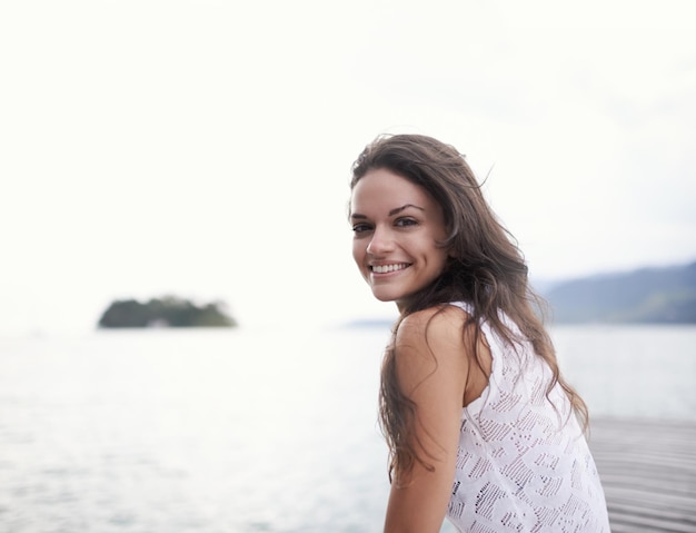 Taking the time out to focus on me Portrait of an attractive young woman sitting on a jetty by the lake