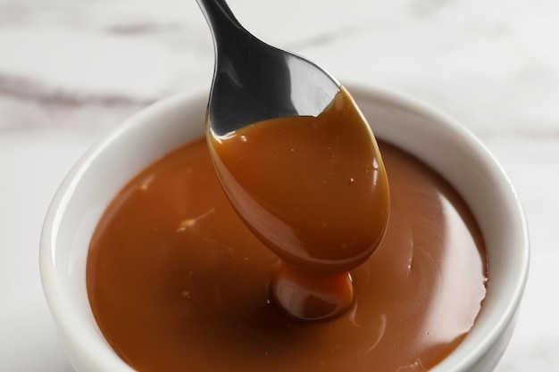 Taking yummy salted caramel with spoon from bowl on table closeup