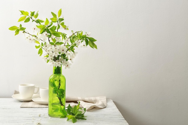 Takken van bloeiende boom bloemen en bladeren in glazen vaas op houten tafel met kopjes