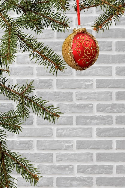 Takken van dennenboom met een bal als kerstversiering met een grijze bakstenen muur op de achtergrond.