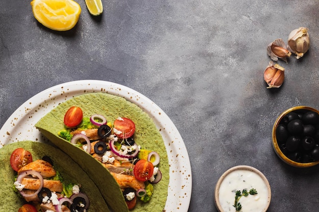 Takos with guacamole, fried chicken, cottage cheese, tomato, red onion, garlic, olives in green
tortilla with basil and spinach. flatlay with copyspace