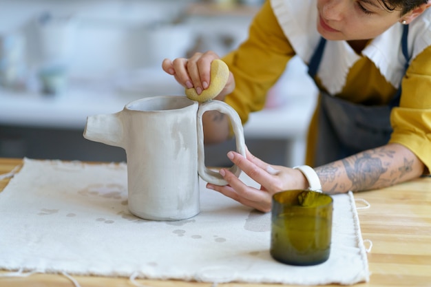 ワークショップスタジオで生の粘土からセラミック水差しを形作る陶芸家の女性の仕事で才能のある職人