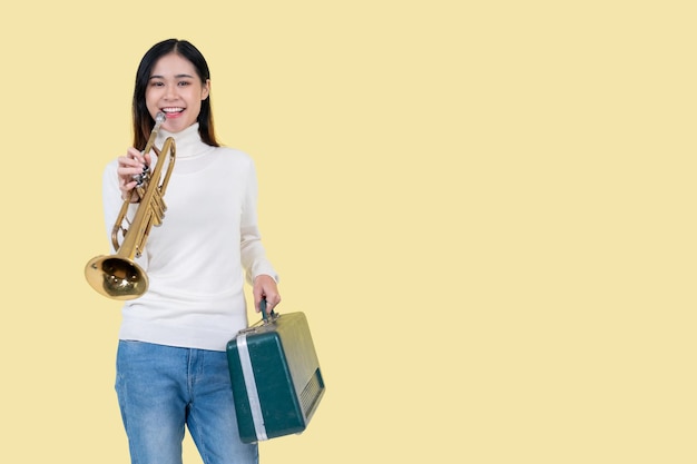 A talented Asian woman is holding the trumpet while standing against an isolated yellow background