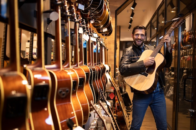 彼が音楽店で購入したい新しいギター楽器をチェックしてテストする革のジャケットの才能のある白人ミュージシャン。