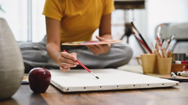 Foto artista femminile di talento che tiene il pennello disegnando e dipingendo la sua opera d'arte su una tela bianca