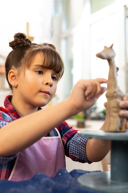 Talented girl modeling clay giraffe at the art lesson