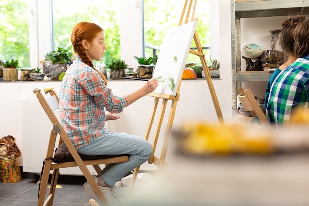 Talented girl sitting near drawing easel and coloring picture