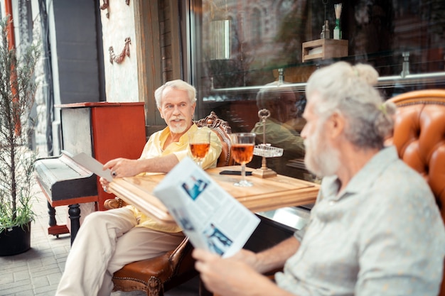 Talking to brother. Bearded grey-haired man reading news and talking to brother