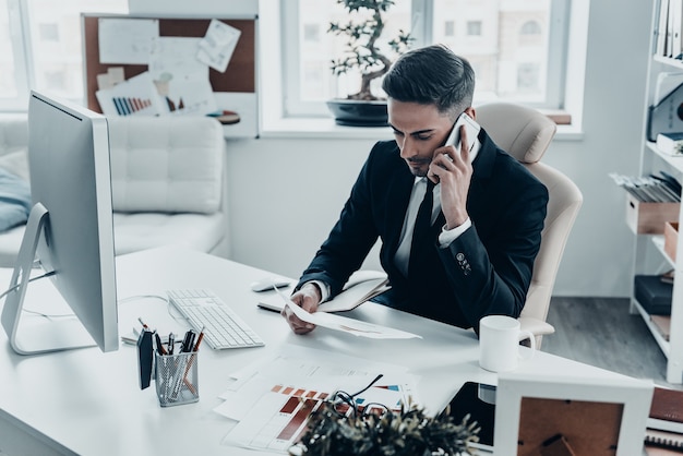 Talking business details. Handsome young man in full suit talking on the phone 