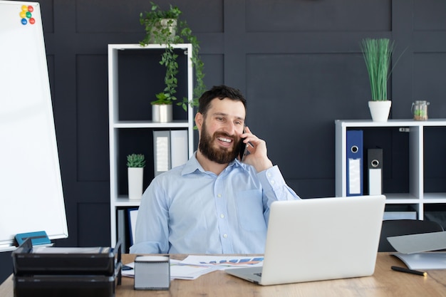 Talking business details. Handsome young man  talking on the phone while sitting at the office desk