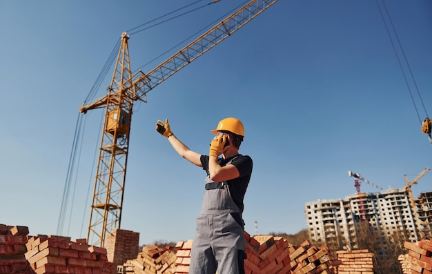 Talking by phone Construction worker in uniform and safety equipment have job on building