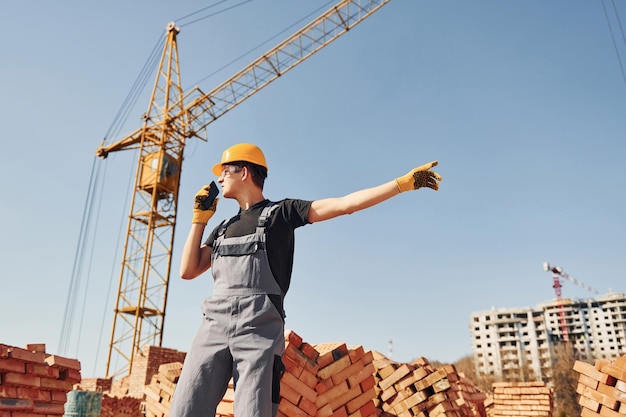 Talking by phone Construction worker in uniform and safety equipment have job on building