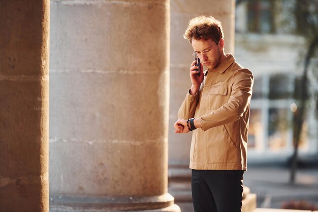 Talking by phone Elegant young man in formal classy clothes outdoors in the city