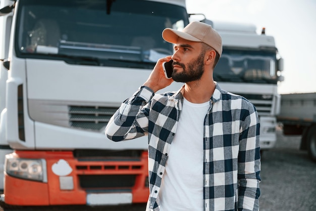 Talking by phone Young truck driver is with his vehicle at daytime