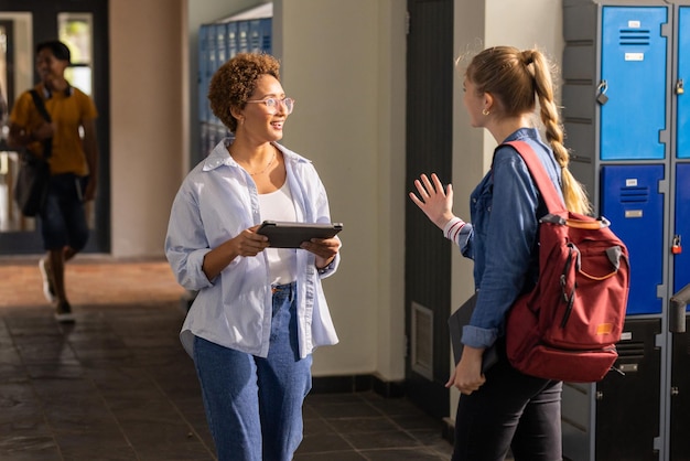 talking in high school hallway two teenage girls with tablet and backpack near lockers