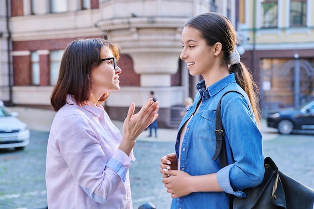 Photo talking mom and teenage daughter outdoors on a city street parents and child teenager laughing smiling walking together family two generations lifestyle leisure people concept