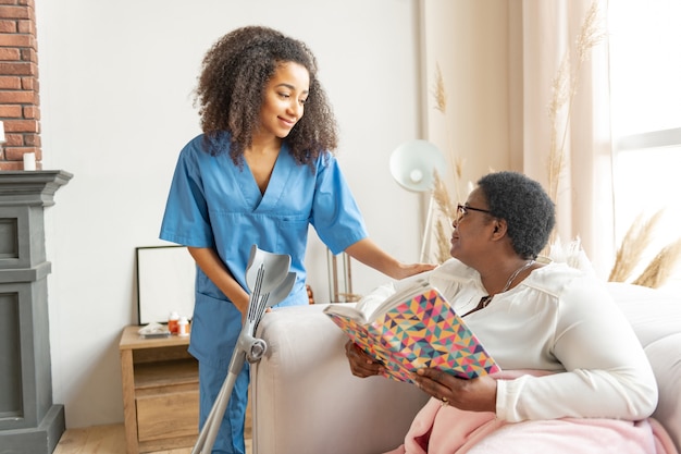 Talking to nurse. Dark-eyed woman with short hair cut wearing glasses reading the book and talking to nurse